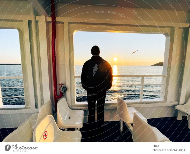 Ein Mann steht an der Reling einer Fähre und blickt übers Meer auf den Sonnenaufgang Möwen beobachten Überfahrt Passagierschiff Ausflug An Bord Freiheit