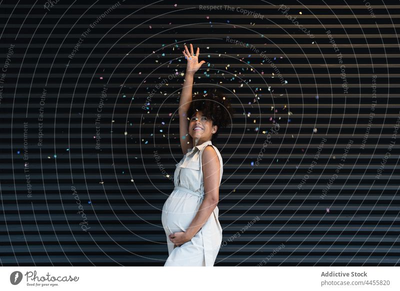 Glückliche schwarze schwangere Frau, die Konfetti wirft vorwegnehmen werfen feiern positiv mütterlich warten Bauch farbenfroh Schwangerschaft erwarten Unterleib