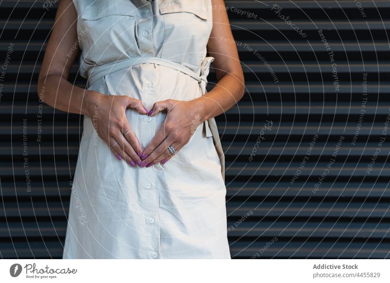 Anonyme schwarze Frau zeigt Herz-Geste auf schwangeren Bauch gestikulieren mütterlich Glück erwarten vorwegnehmen pränatal positiv Schwangerschaft Unterleib