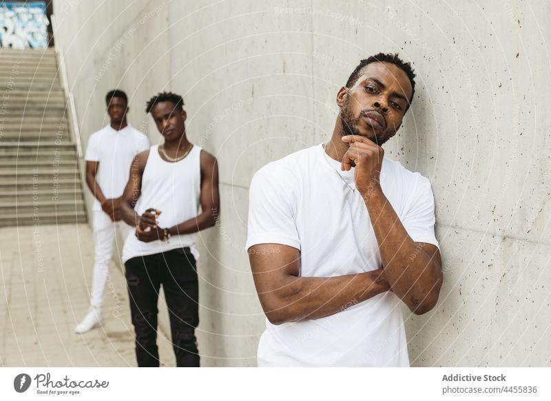 Schwarze männliche Freunde in stilvollen Outfits stehen in der Nähe einer Betonwand Männer cool Stil maskulin trendy modern selbstbewusst nachdenklich