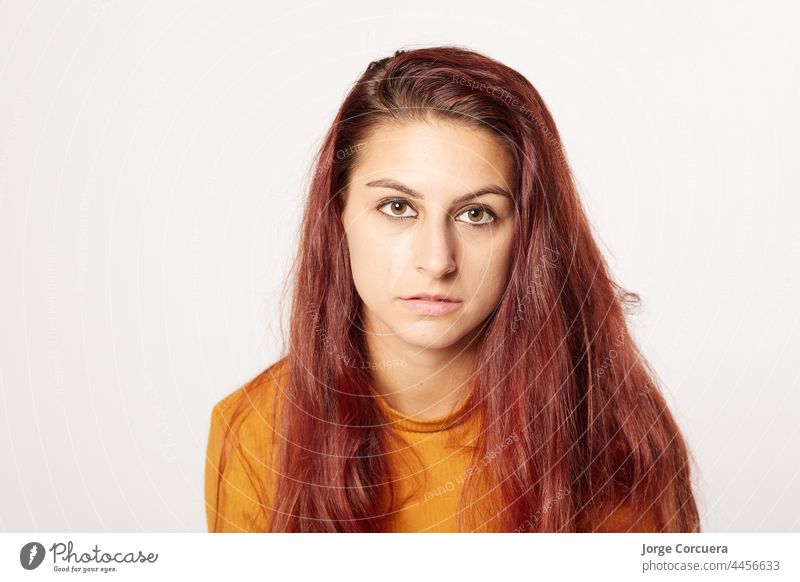 schönes 20-jähriges Mädchen, das mit neutralem Gesichtsausdruck intensiv in die Kamera schaut. Schöne rote Frisur und orangefarbenen Pullover Haut Teenager