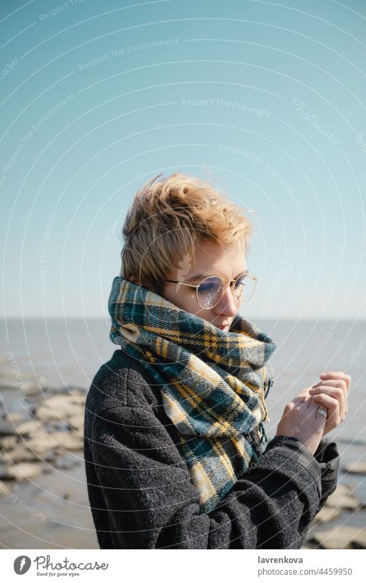Junge Frau mit Brille wärmt sich an einem Strand allein Herbst Kaukasier Mantel kalt Gesicht fallen Hände Lifestyle Natur im Freien Person Porträt Seeküste