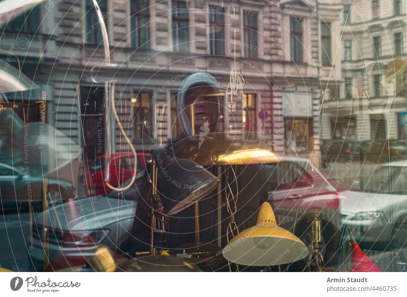 Das Spiegelbild eines jungen Mannes in einem Schaufenster mit alten Lampen Porträt Reflexion & Spiegelung Kapuzenpulli Straße urban Werkstatt Fenster Vitrine
