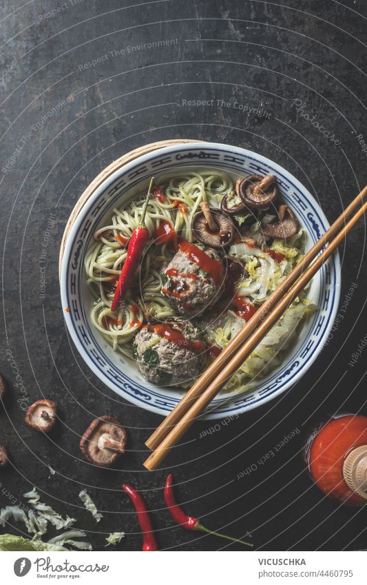 Leckeres asiatisches Essen Schüssel mit Ramen-Nudeln, Fleischbällchen, Gewürze und Essstäbchen auf dunklem Hintergrund. Ansicht von oben geschmackvoll