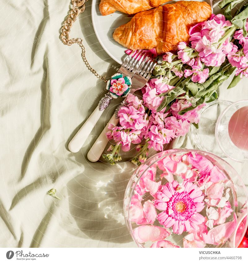 Ästhetisches Frühstück mit Croissant und rosa Blumenstrauß auf hellgrüner Decke bei Sonnenschein. Ansicht von oben Ästhetik Haufen Licht Draufsicht Hintergrund