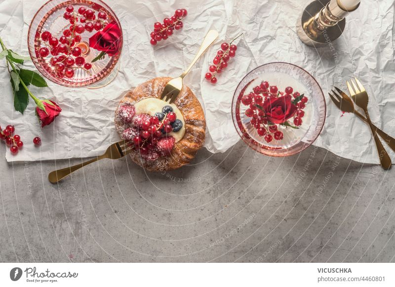 Romantischer Hintergrund mit zwei Gläsern Champagner mit roten Beeren und süßen Pudding Brötchen, mit zwei goldenen Gabeln, Beeren und Blumen. Ansicht von oben