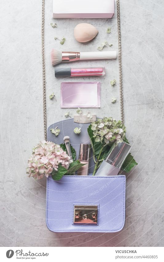 Kleine fliederfarbene Handtasche mit Hortensienblüten und verschiedenen Kosmetika. Schönheitskonzept wenig Fliederbusch Blumen Konzept schön Zubehör Hintergrund
