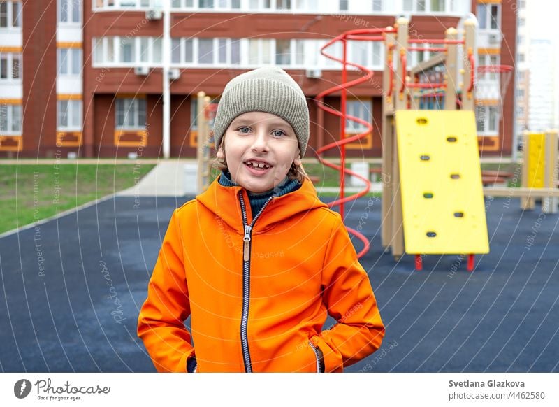 Lustiger kaukasischer blonder Junge in einer orangefarbenen Jacke spielt auf dem Sportplatz Glück Kindheit Spielplatz im Freien Teenager Lächeln Spaß Kaukasier