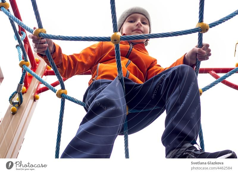 Lustiger kaukasischer blonder Junge in einer orangefarbenen Jacke spielt auf dem Sportplatz Glück Kindheit Spielplatz im Freien Teenager Lächeln Spaß Kaukasier