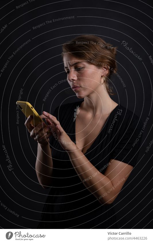 Eine junge schöne Frau mit einem Smartphone in einem Studio Schuss in schwarzem Kleid und Hintergrund 20-25 Erwachsener attraktiv Schönheit brünett lässig