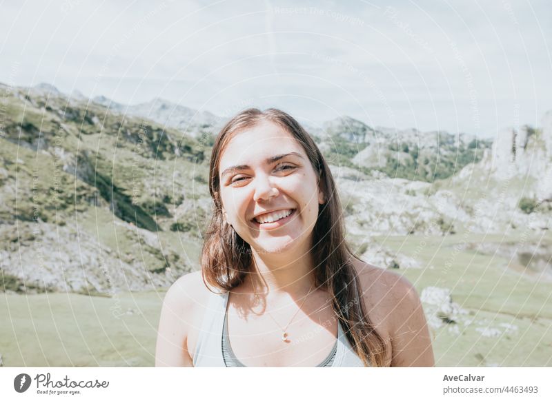 Porträt einer jungen lächelnden Frau, deren Gesicht teilweise mit fliegenden Haaren bedeckt ist, an einem windigen Tag am Berg stehend - sorglose Frau Genuss
