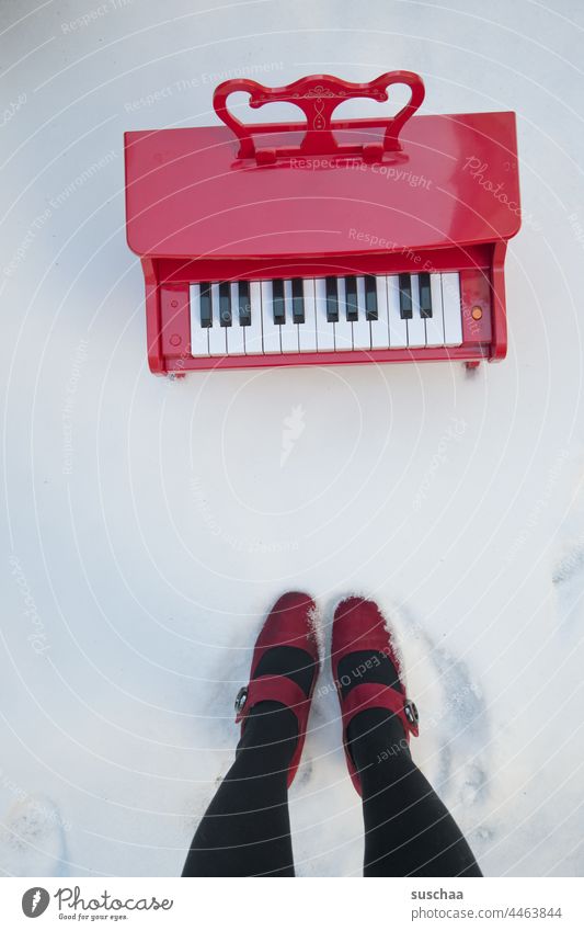 kinderklavier im schnee, daneben beine einer lady Kinderklavier rot Schnee Winter kalt rote Damenschuhe Beine Füße stehend kurios Tasten Klaviertasten Musik