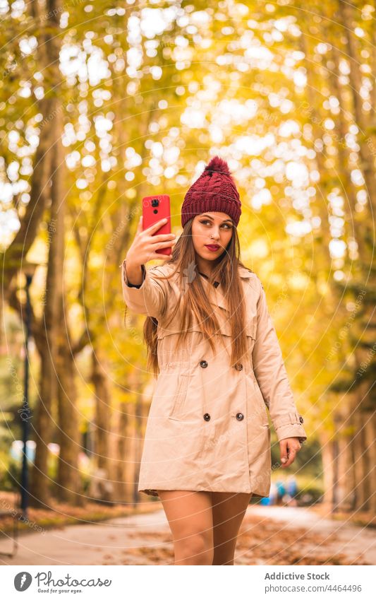 Frau macht Selfie mit Smartphone im Herbstpark Stil benutzend Park Gasse fallen feminin Trenchcoat Selbstportrait Telefon fotografieren Baum Mobile Gerät