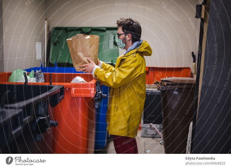Mann mit Gesichtsmaske wirft Müll in einen Container Müllcontainer Öko Hausarbeit Müllsack Tasche wiederverwenden Werfen grün Ökologie Coronavirus Verklappung