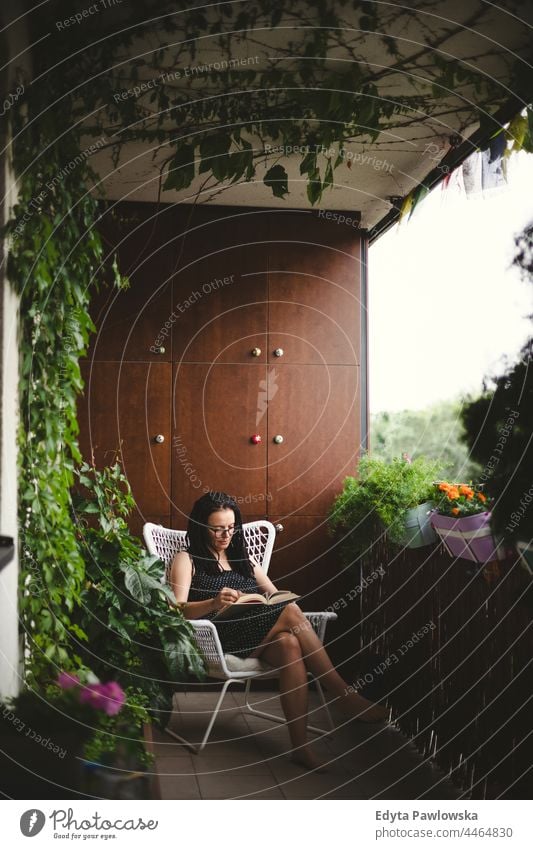 Frau liest ein Buch auf einem grünen Balkon Rastalocken Efeu Blumen Balkon Garten bequem zu Hause bleiben Quarantäne aussruhen Natur gemütlich Terrasse Lesebuch