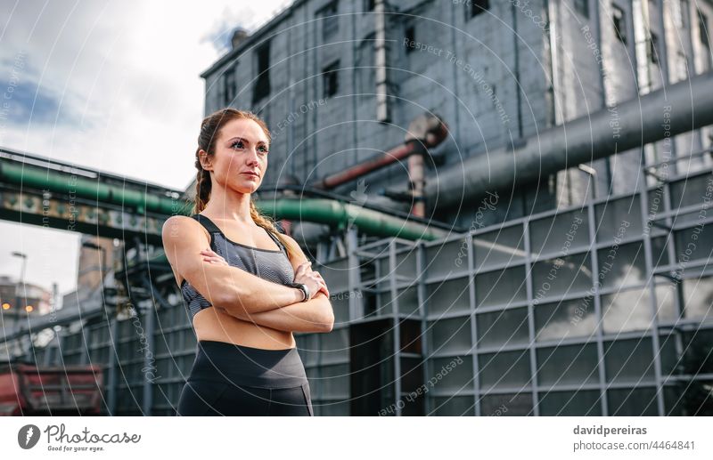 Sportlerin mit verschränkten Armen in Pose vor einer Fabrik Gewerbegebiet sportlich Frau Textfreiraum Läufer verschränkte Arme attraktiv Jogger ernst