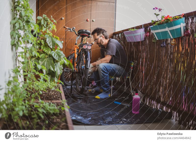 Mann repariert sein Fahrrad auf einem Balkon Fahrrad reparieren urban Natur Lifestyle Freizeit Kaukasier jung Großstadt arbeiten Porträt Pflanze Person männlich