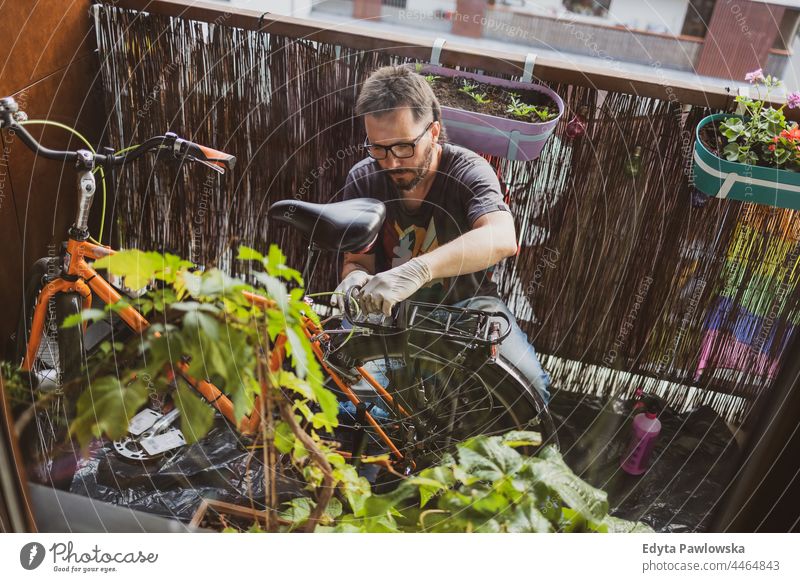 Mann repariert sein Fahrrad auf einem Balkon Fahrrad reparieren urban Natur Lifestyle Freizeit Kaukasier jung Großstadt arbeiten Porträt Pflanze Person männlich