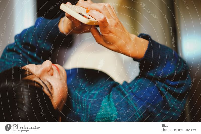 2500 / Eine Frau mit ihrem Smartphone in der Hand liegen Handy Telefon tippen entspannt texten Mobile braunhaarig handysüchtig Lifestyle Pullover