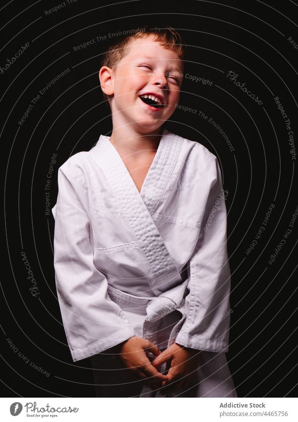 Fröhliches Kind in weißer Kimono-Uniform lachend im Atelier Junge Karate expressiv Lachen Spaß Witz Freude lustig Mund geöffnet spielerisch Spaß haben