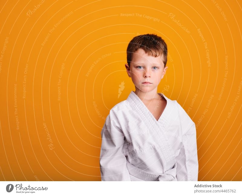 Seriöser Junge in Kimono-Uniform in hellem Studio stehend Karate Sport kämpferisch ernst Mut starren Aktivität Gefecht Kämpfer Kind Kindheit wenig Kultur