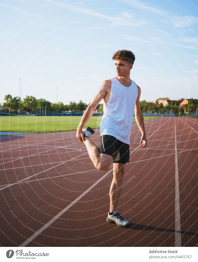 Fit-Sportler streckt sein Bein während des Trainings auf der Bahn Athlet Dehnung Bein angehoben Aufwärmen üben Mann Stadt Übung Turnschuh Sportbekleidung passen