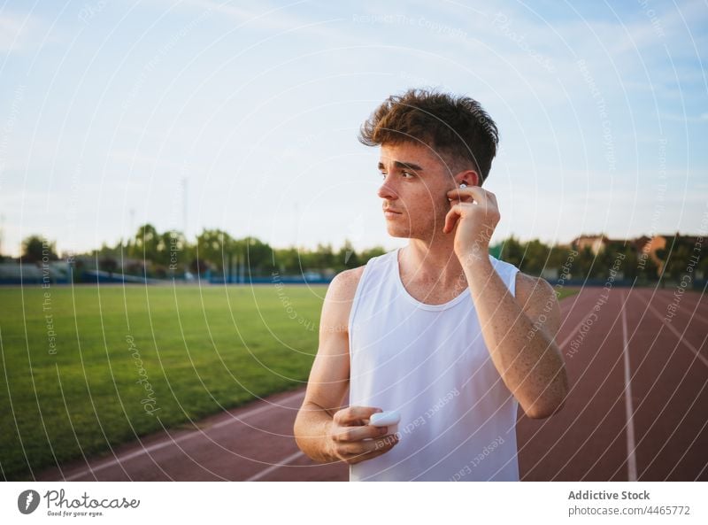 Sportler, der auf der Rennstrecke ein Lied aus einem Ohrhörer hört Athlet Ohrstöpsel zuhören Musik Gesang nachdenken Leichtathletik Mann benutzend Apparatur