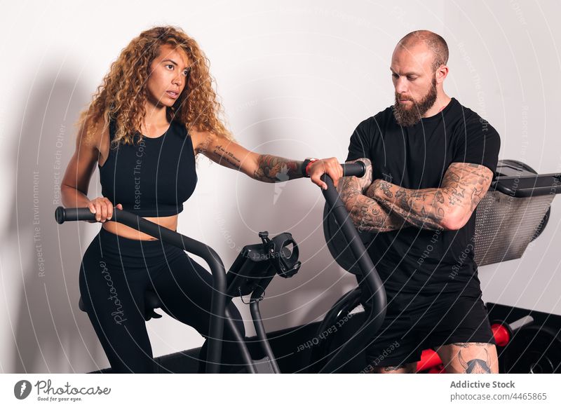 Sportlerin beim Ausdauertraining mit Ausbilderin hispanisch Mischrennen Herz Training Fitnessstudio Maschine Gerät Zyklus Trainerin Aktivität Frau Übung