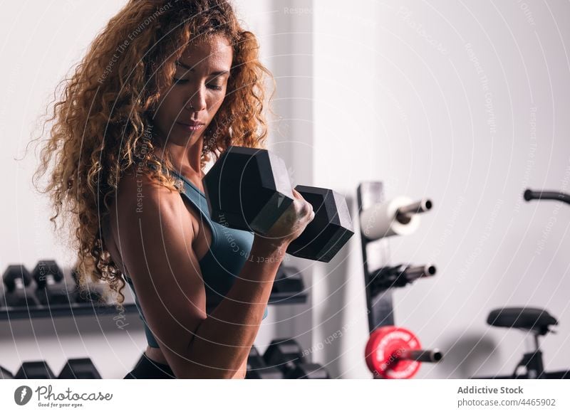Konzentrierte Sportlerin beim Training mit Kurzhanteln im Fitnessstudio hispanisch Mischrennen Bizeps Übung stark physisch Frau muskulös Locken passen Aktivität