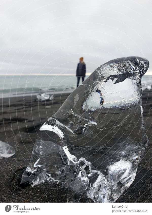 Transparentes Gletschereis, das am Diamond Beach, Island, an Land gespült wurde, mit einer Person im Hintergrund Strand schwarzer Strand schwarzer Sand blau