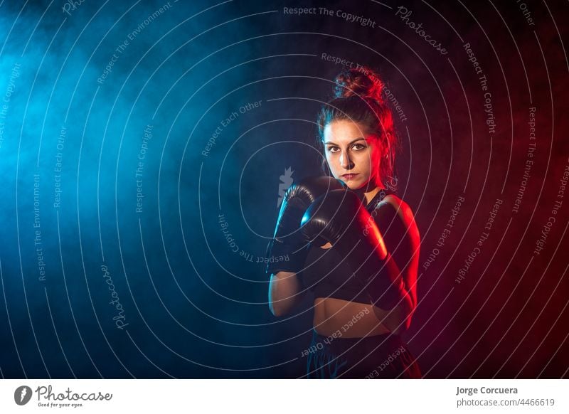 Junge Frau beim Boxtraining im Fitnessstudio, sie trägt Boxhandschuhe Boxsport Boxer Fokus Training passen Athlet Sportbekleidung Herausforderung Gerät