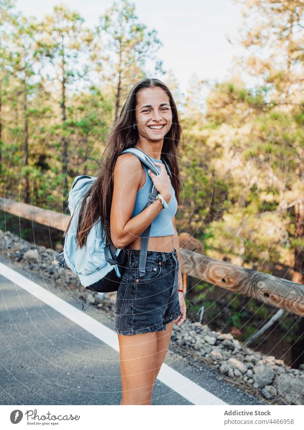 Teenager mit Rucksack überquert Straße gegen Bäume Reisender durchkreuzen Natur Baum Route achtsam Umwelt Ökologie Insel Zaun Spaziergang Asphalt Fahrbahn