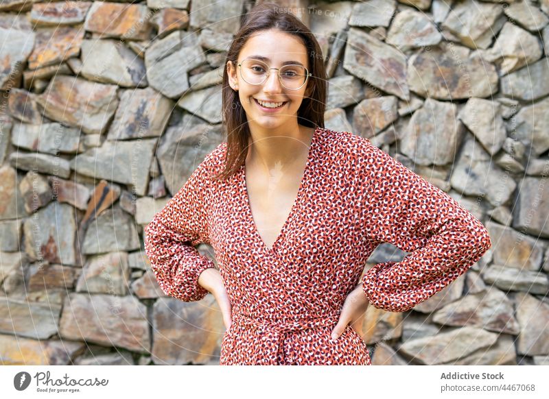 Positiv, weiblich, stehend mit den Händen auf der Hüfte gegen eine Steinmauer Frau Lachen Glück heiter Lächeln froh brünett positiv jung Stil Steinwand