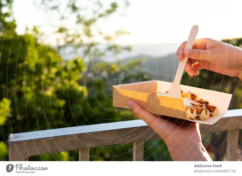 Anonyme Person genießt leckere Waffeln vor dem Hintergrund der Berge im Sonnenschein essen Dessert Leckerbissen Sahne gepeitscht süß Imbissbude Berge u. Gebirge