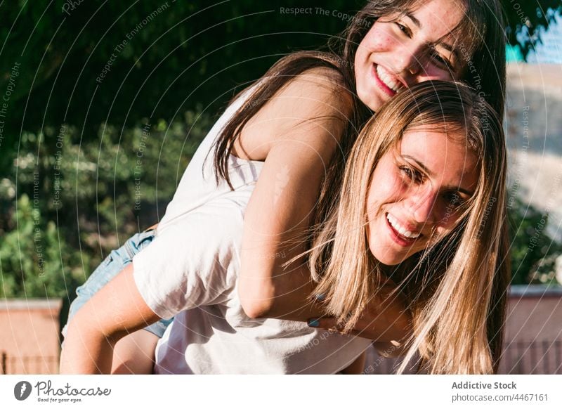 Lächelnder Teenager, der seine Freundin auf der Straße Huckepack trägt heiter Spaß haben Freundschaft Umarmen Zeit verbringen sorgenfrei Porträt Wochenende