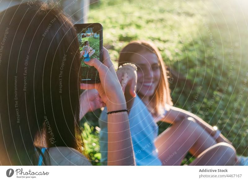 Crop Teenager fotografiert Freundin mit Smartphone im Park bester Freund fotografieren Lächeln Händchenhalten Zeit verbringen Moment Touchscreen benutzend