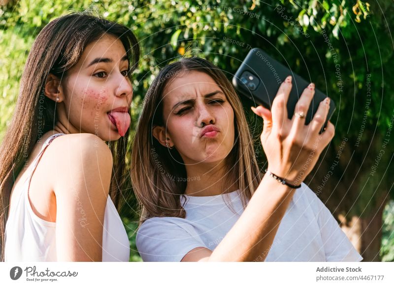 Freundinnen schneiden Grimassen, während sie im Park ein Selfie mit dem Smartphone machen Spaß haben Moment Gedächtnis Freundschaft benutzend Apparatur
