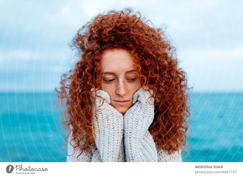 Unglückliche Frau schaut auf das Meer hinunter MEER Persönlichkeit Individualität Porträt Meeresufer lange Haare Freude gestrickt Ingwerhaar Seeküste rote Haare