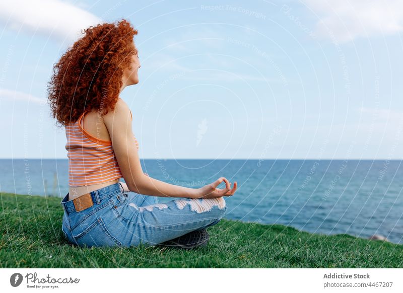 Junge Frau sitzt in Lotus-Pose und meditiert im Gras meditieren MEER Asana Hügel Zen Harmonie Yoga Stressabbau padmasana mental sorgenfrei Sprit Meeresufer