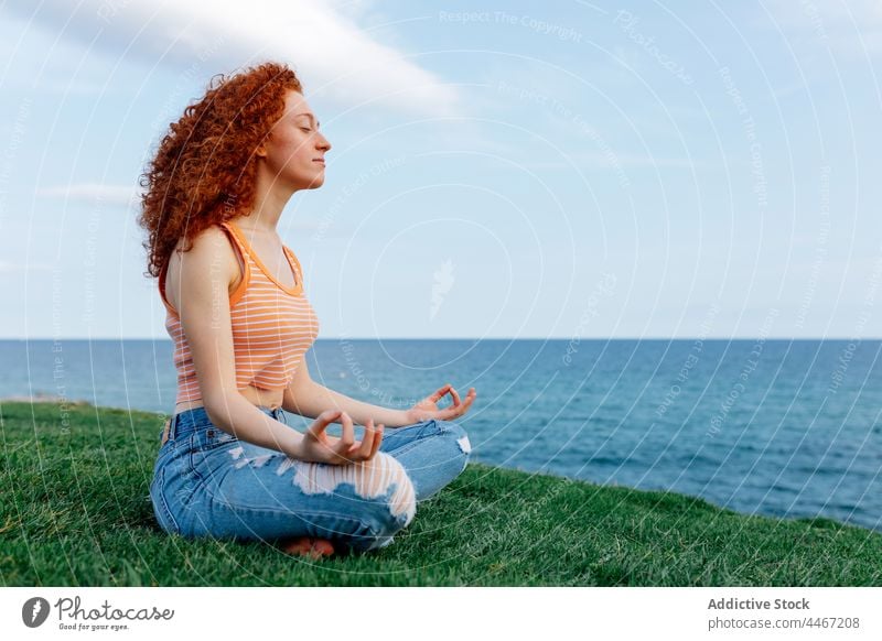 Junge Frau sitzt in Lotus-Pose und meditiert im Gras meditieren MEER Asana Hügel Zen Harmonie Yoga Stressabbau padmasana mental sorgenfrei Sprit Meeresufer
