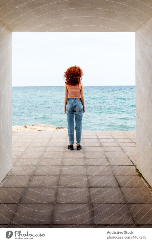 Frau mit lockigem Haar steht in Betonflur am Meer Reisender MEER blau Ausflug bewundern Durchgang Ufer Urlaub Feiertag Natur Küste Tourist reisen Tourismus