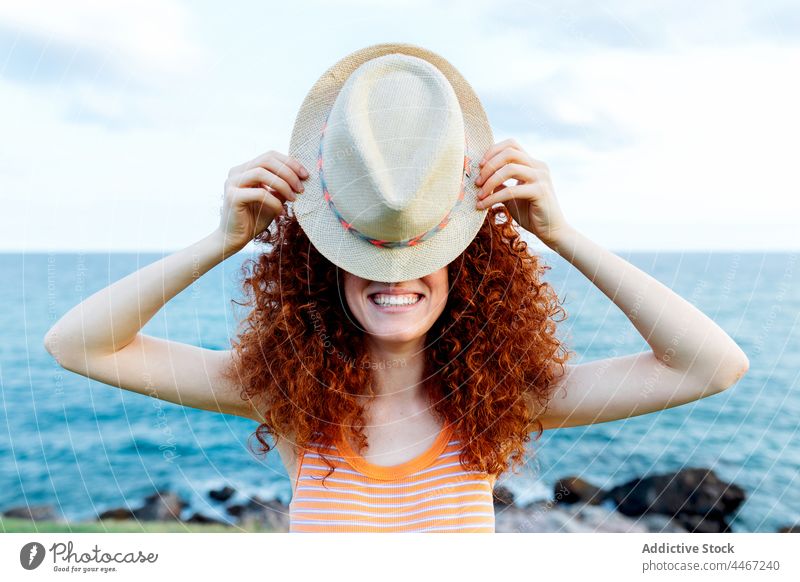 Frau bedeckt Gesicht mit Hut am Meeresufer Tierhaut Deckblatt Küste MEER Körperhaltung spielerisch Natur geheim Locken Rotschopf Wasser Feiertag Ufer rote Haare