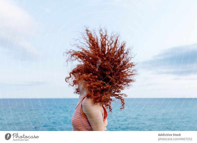 Entspannte Frau, die ihr lockiges Haar am Meeresufer auspeitscht MEER Haare schütteln Kälte Energie sorgenfrei Freiheit sich[Akk] entspannen Ufer Bewegung