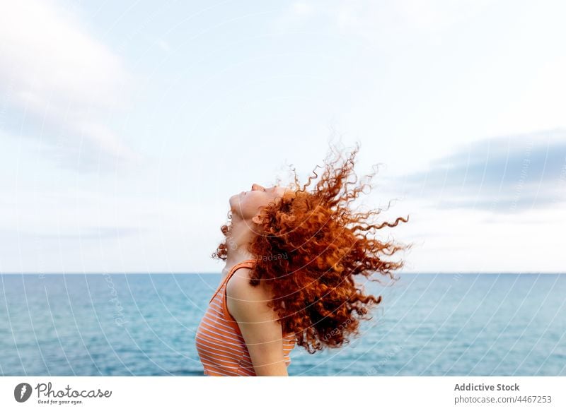 Entspannte Frau, die ihr lockiges Haar am Meeresufer auspeitscht MEER Haare schütteln Kälte Energie sorgenfrei Freiheit sich[Akk] entspannen Ufer Bewegung