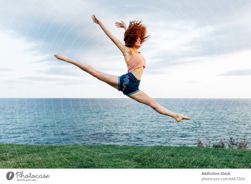 Flexible Frau springt anmutig auf grasbewachsenem Meeresufer Split Dehnung springen MEER Körperhaltung Aktion beweglich Glück Küste Freiheit über der Erde