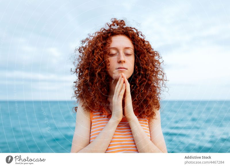 Frau mit Händen auf der Brust meditiert am Meeresufer MEER Augen geschlossen Strand Yoga meditieren gestikulieren Sprit Namaste mental Stressabbau Harmonie