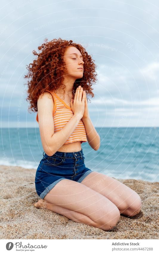 Frau mit Händen auf der Brust beim Meditieren am Sandstrand MEER Strand Yoga meditieren gestikulieren Sprit Namaste mental Stressabbau Harmonie Achtsamkeit