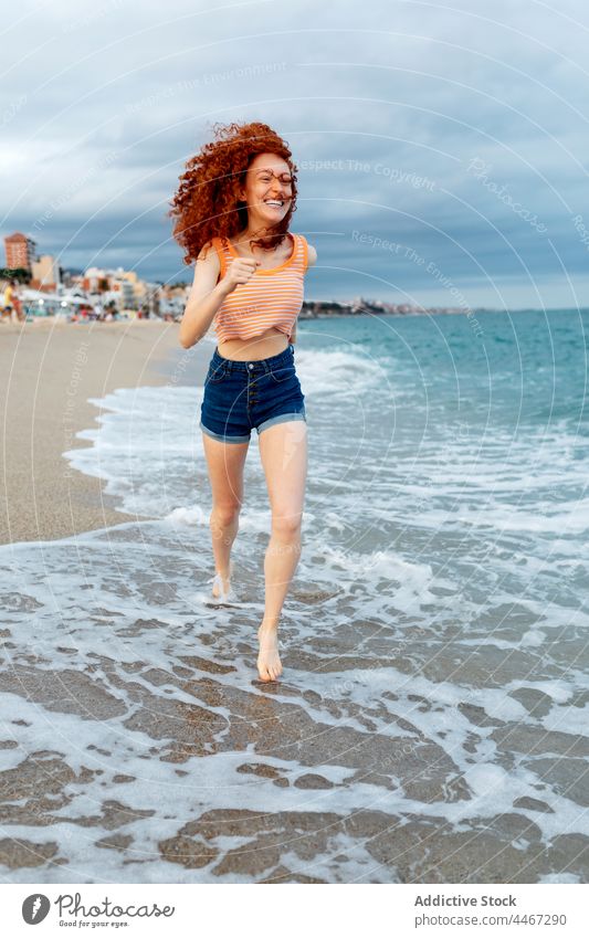 Fröhliche Frau läuft am sandigen Meeresufer Strand laufen MEER Sand Wind Glück genießen winken schäumen reisen Wasser sorgenfrei fliegendes Haar Freiheit Küste