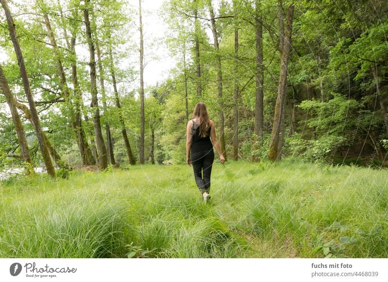 Junge Frau läuft über eine Wiese in einem Wald, Frau in der Natur Outdoor Rücken lange Haare brünett Leggings Spaziergang grün Bäume frische Luft sommer schwarz