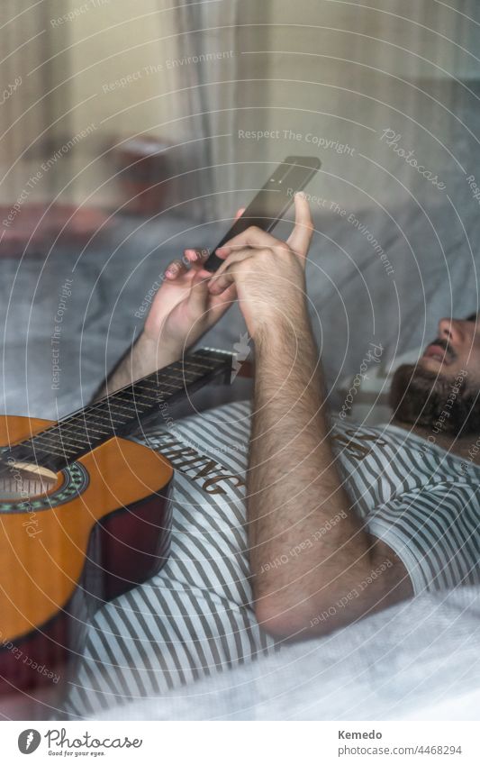 Blick durch ein Fenster auf einen Mann mit Gitarre, der auf dem Sofa liegt und ein Telefon benutzt Intimität Privatsphäre Technik & Technologie Zelle